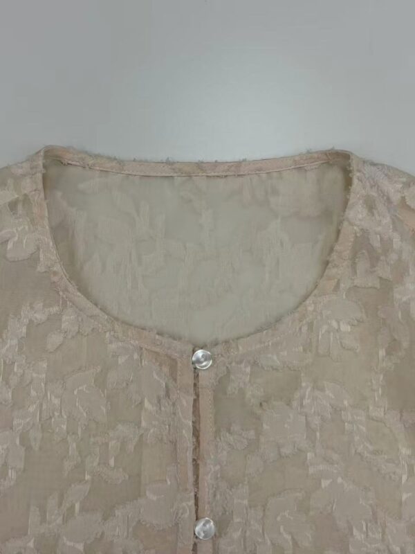 Close-up of a beige lace blouse with a round neckline and pearl button closure, perfect for formal or casual occasions.