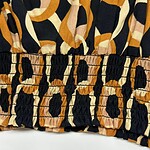 Close-up of fabric with bold animal print pattern in black, beige, and orange tones, featuring gathered elastic detail at the bottom edge.