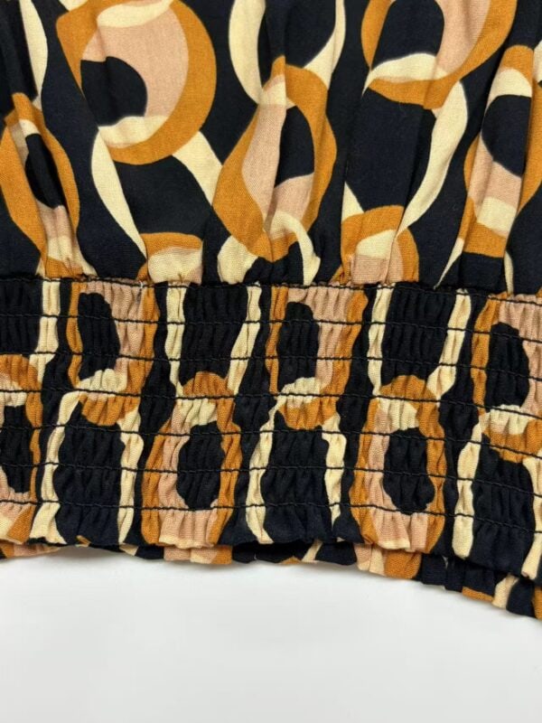 Close-up of fabric with bold animal print pattern in black, beige, and orange tones, featuring gathered elastic detail at the bottom edge.