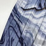 Close-up of a blue fabric with intricate black and white geometric patterns, suitable for stylish clothing or accessories.