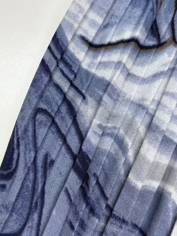 Close-up of a blue fabric with intricate black and white geometric patterns, suitable for stylish clothing or accessories.