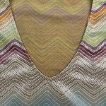 Close-up of a colorful woven fabric with a V-neck design, featuring zigzag patterns in yellow, purple, green, and beige tones, suitable for fashion and textile enthusiasts.