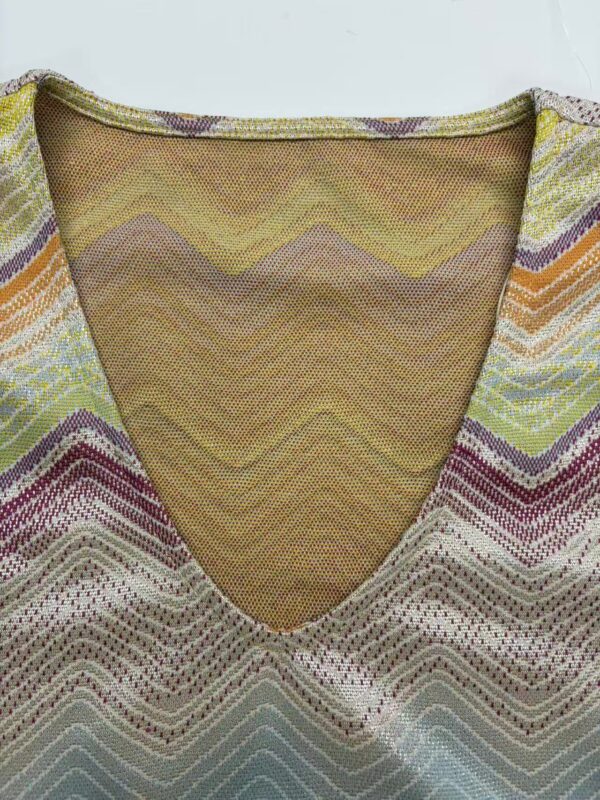 Close-up of a colorful woven fabric with a V-neck design, featuring zigzag patterns in yellow, purple, green, and beige tones, suitable for fashion and textile enthusiasts.