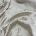 Close-up of luxurious cream satin fabric with smooth, shiny surface and soft drape, ideal for high-end clothing and fashion design.