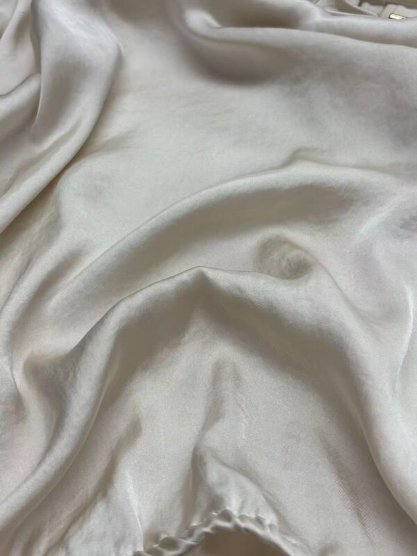 Close-up of luxurious cream satin fabric with smooth, shiny surface and soft drape, ideal for high-end clothing and fashion design.