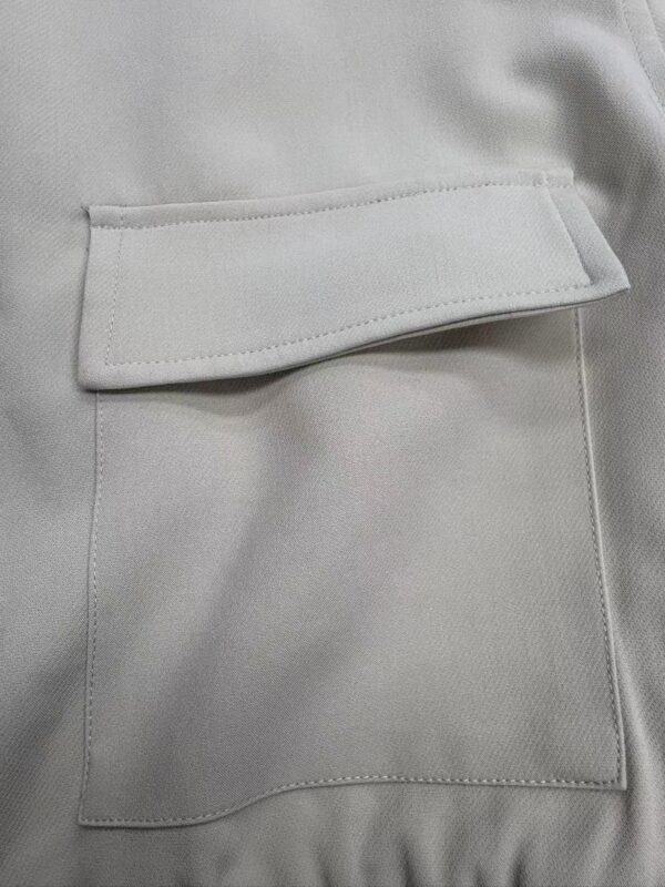 Close-up of a light grey fabric with a stylish pocket featuring a flap, showcasing high-quality material and craftsmanship.