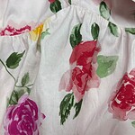 Close-up of a floral dress featuring pink, purple, and green watercolor-style flowers on white fabric, highlighting the fabric's texture and vibrant colors.