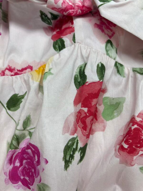 Close-up of a floral dress featuring pink, purple, and green watercolor-style flowers on white fabric, highlighting the fabric's texture and vibrant colors.