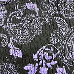 Close-up of fabric featuring intricate purple floral and geometric patterns on a black background, showcasing detailed textile design.