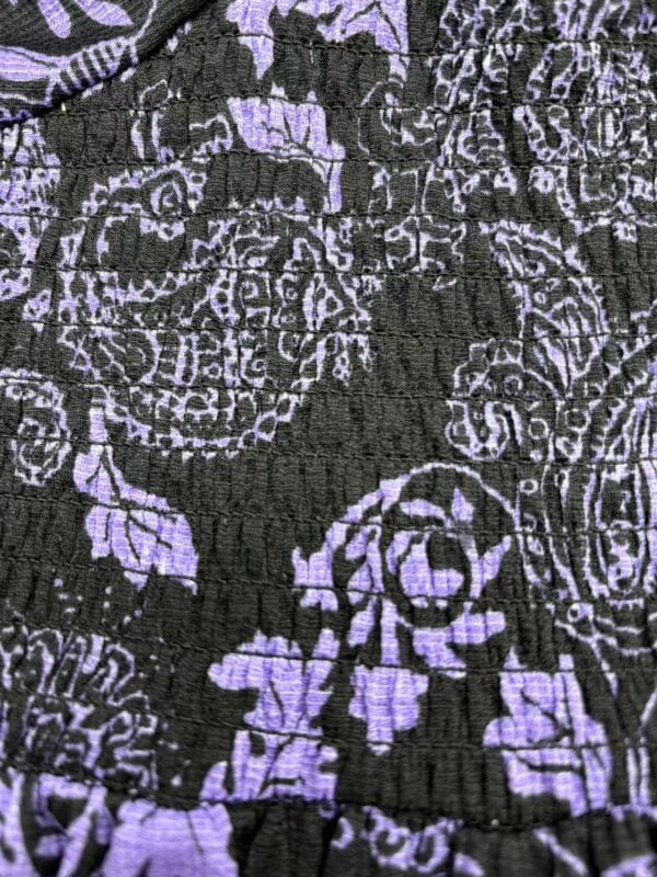 Close-up of fabric featuring intricate purple floral and geometric patterns on a black background, showcasing detailed textile design.