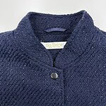 Close-up of a navy blue tweed women's jacket with a high collar and a single button closure, showcasing textured fabric and stylish design.