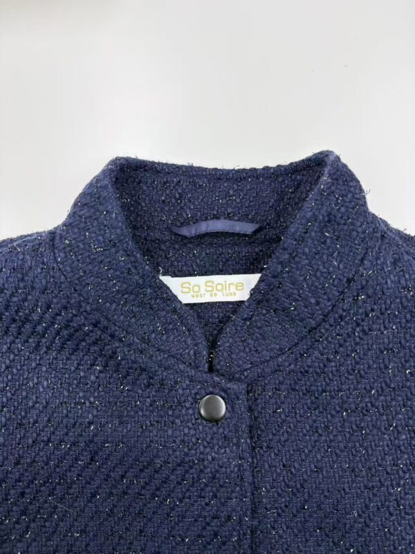 Close-up of a navy blue tweed women's jacket with a high collar and a single button closure, showcasing textured fabric and stylish design.