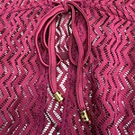 Close-up of a pink lace dress featuring a drawstring with gold tips, showcasing intricate zigzag lace pattern and delicate fabric texture.