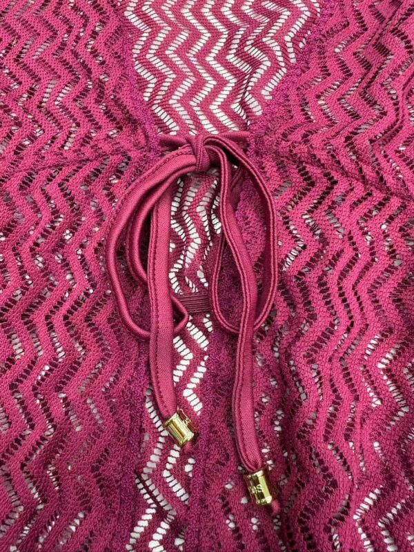 Close-up of a pink lace dress featuring a drawstring with gold tips, showcasing intricate zigzag lace pattern and delicate fabric texture.