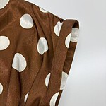 Close-up of a brown satin dress with large white polka dots, showcasing the fabric's texture and the sleeve design.
