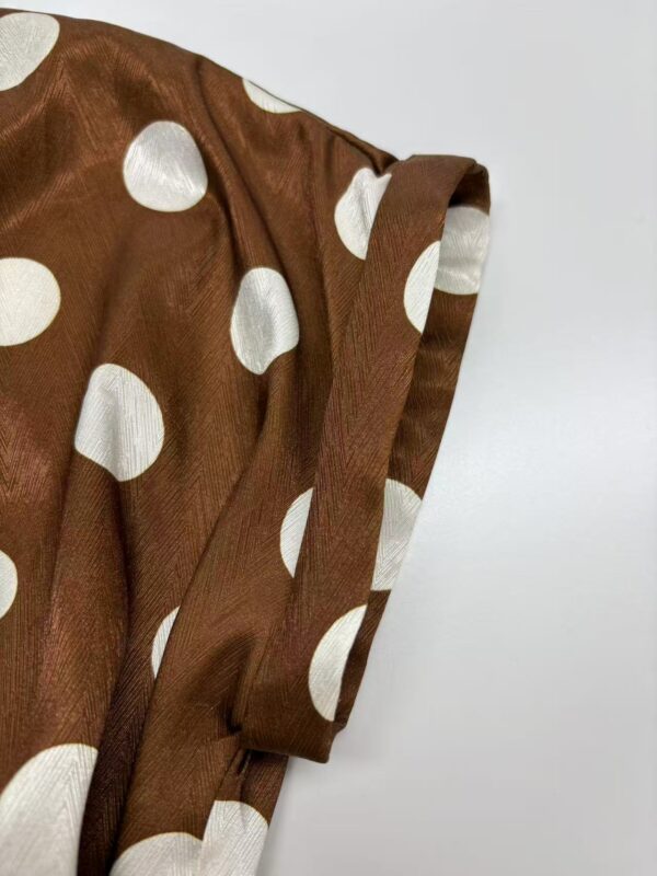 Close-up of a brown satin dress with large white polka dots, showcasing the fabric's texture and the sleeve design.
