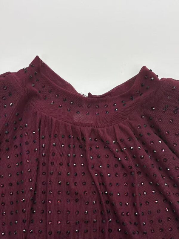 Close-up of a burgundy blouse featuring rhinestone embellishments on the neckline and pleated fabric details for a stylish look.