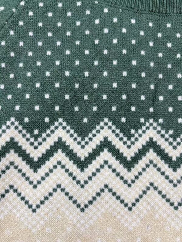 Close-up of a green knitted sweater with white geometric and zigzag patterns, perfect for holiday fashion and winter wear.