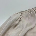 Close-up of a beige satin blouse with puffed sleeves, showcasing smooth fabric and stylish design, perfect for fashion-forward women.