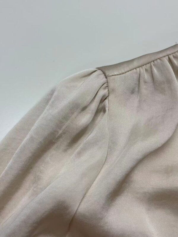 Close-up of a beige satin blouse with puffed sleeves, showcasing smooth fabric and stylish design, perfect for fashion-forward women.
