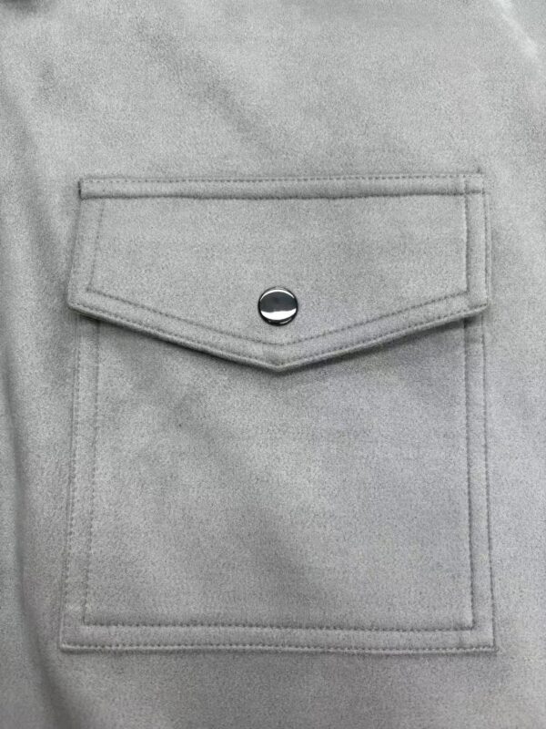 Close-up of a light grey denim jacket pocket with a silver button, showcasing casual fashion style.