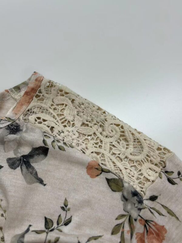 Close-up of a floral dress featuring a delicate lace trim on the shoulder, showcasing elegant fabric and intricate design for fashion and style.