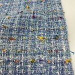 Close-up of a textured tweed fabric featuring a mix of blue, white, and multicolored threads, showcasing detailed weave and colorful accents.