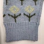 Close-up of a knitted sweater featuring a geometric pattern with yellow and black diamond shapes on a light blue background.