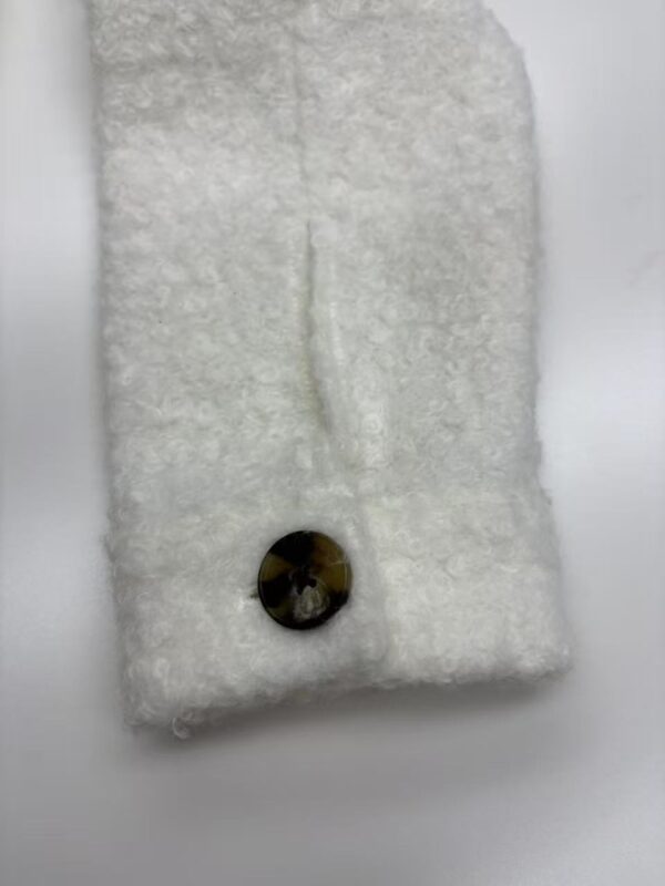 Close-up of a white wool scarf featuring a decorative black button, showcasing soft texture and stylish design for fashion accessories.