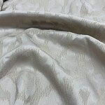 Close-up of luxurious cream silk fabric with subtle pattern, ideal for high-end fashion and couture designs.