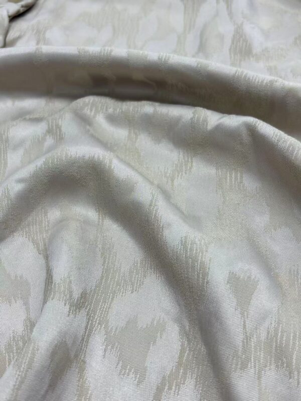 Close-up of luxurious cream silk fabric with subtle pattern, ideal for high-end fashion and couture designs.