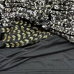 Close-up of layered fabric featuring floral, gold, and black patterns, showcasing intricate design details and textures.