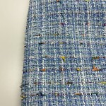 Close-up of vibrant tweed fabric with multicolored threads and textured weave, ideal for high-end fashion garments and accessories.