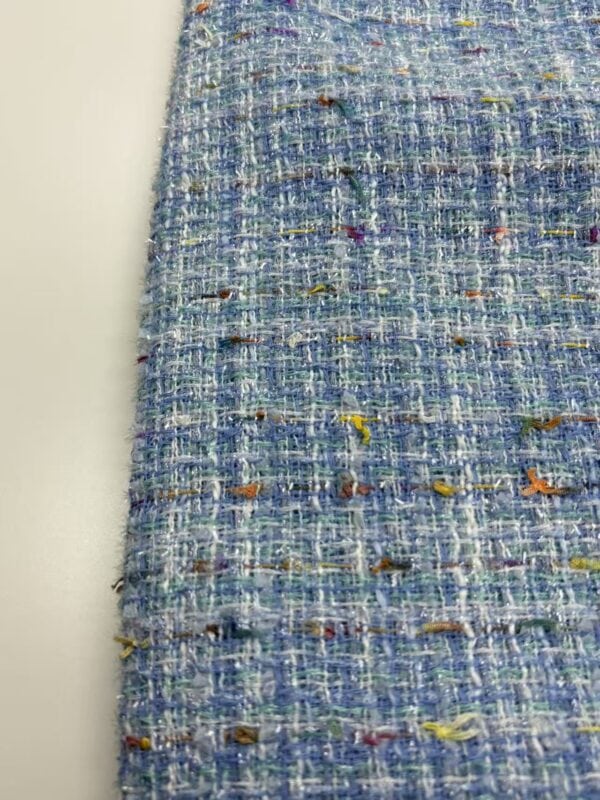 Close-up of vibrant tweed fabric with multicolored threads and textured weave, ideal for high-end fashion garments and accessories.