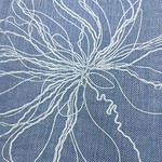 Close-up of blue fabric with intricate white embroidery forming a floral pattern, showcasing fine craftsmanship and detailed textile design.