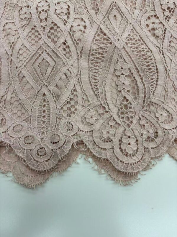 Close-up of intricate beige lace fabric with floral and geometric patterns, ideal for fashion and bridal wear.