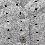 Close-up of a gray knit sweater with black polka dots and gray buttons, showcasing soft fabric and stylish design.