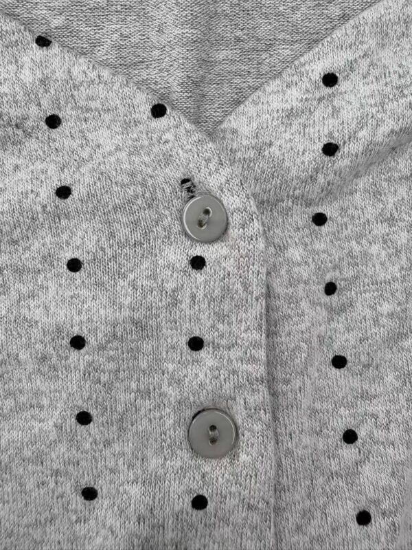 Close-up of a gray knit sweater with black polka dots and gray buttons, showcasing soft fabric and stylish design.