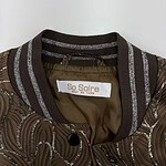 Close-up of a brown bomber jacket with intricate embroidery and striped ribbed collar, featuring a label that reads 'So Soire' for fashion and style.