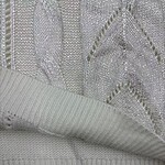 Close-up of white knit fabric with intricate patterns and textured details, showcasing high-quality craftsmanship and fine material suitable for fashion apparel.