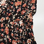 Close-up of a women's dress with a black background and a detailed floral pattern in shades of red, orange, and beige.