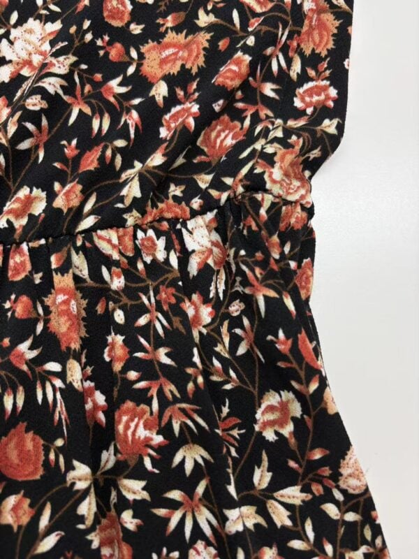 Close-up of a women's dress with a black background and a detailed floral pattern in shades of red, orange, and beige.