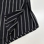 Close-up of a black skirt with white vertical pinstripes, featuring a tied knot detail and a frayed hem, suitable for fashion and style keywords.