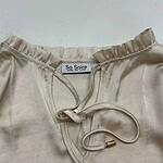 Close-up of a cream satin pajama top with a drawstring neckline and ruffled collar, perfect for stylish loungewear.