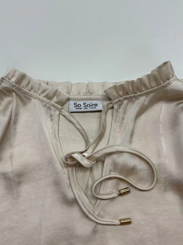 Close-up of a cream satin pajama top with a drawstring neckline and ruffled collar, perfect for stylish loungewear.