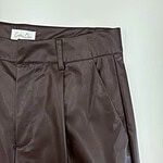 Close-up of stylish brown leather pants with tailored fit, front pleats, and belt loops, perfect for fashion-forward women seeking sophisticated apparel.