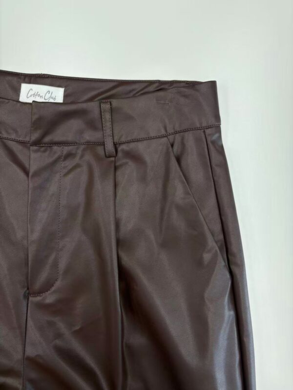 Close-up of stylish brown leather pants with tailored fit, front pleats, and belt loops, perfect for fashion-forward women seeking sophisticated apparel.