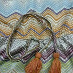 Vibrant handwoven textile featuring zigzag patterns in blue, yellow, purple, and green with decorative tassels in orange and pink.