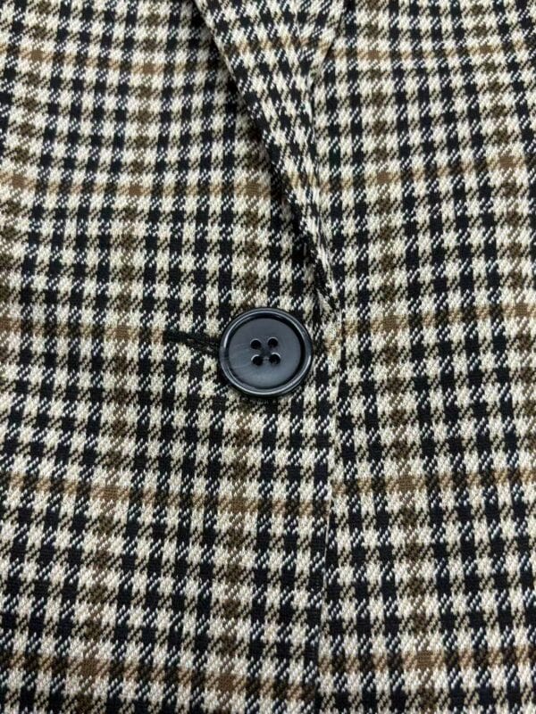 Close-up of a houndstooth patterned coat with a black button, showcasing classic fashion style and high-quality fabric suitable for stylish winter wear.