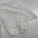 Close-up of white eyelet lace fabric with floral and circular patterns, showcasing intricate embroidery and scalloped edges.